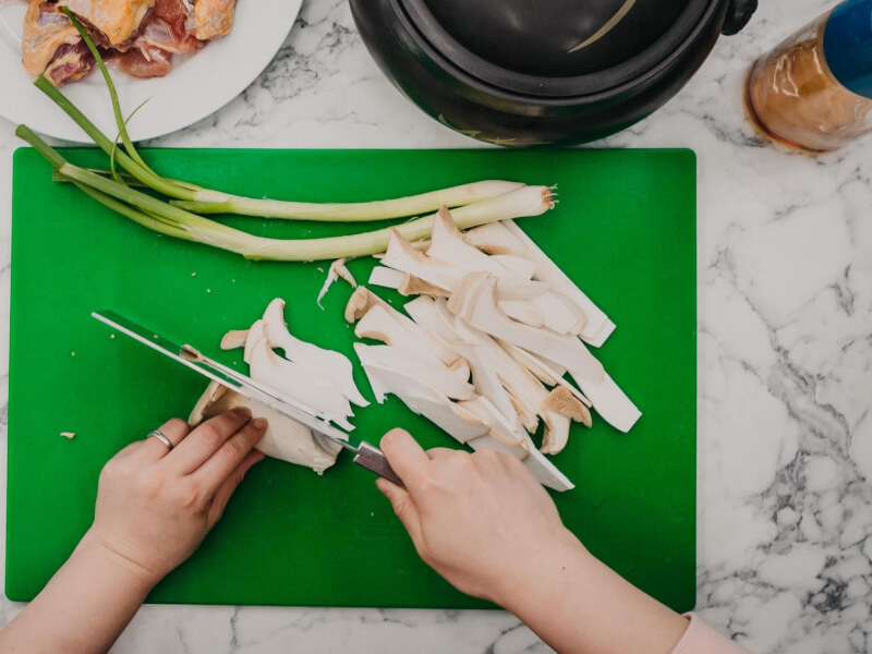 Overhead shot of a person slicing large mushrooms on a green cutting board